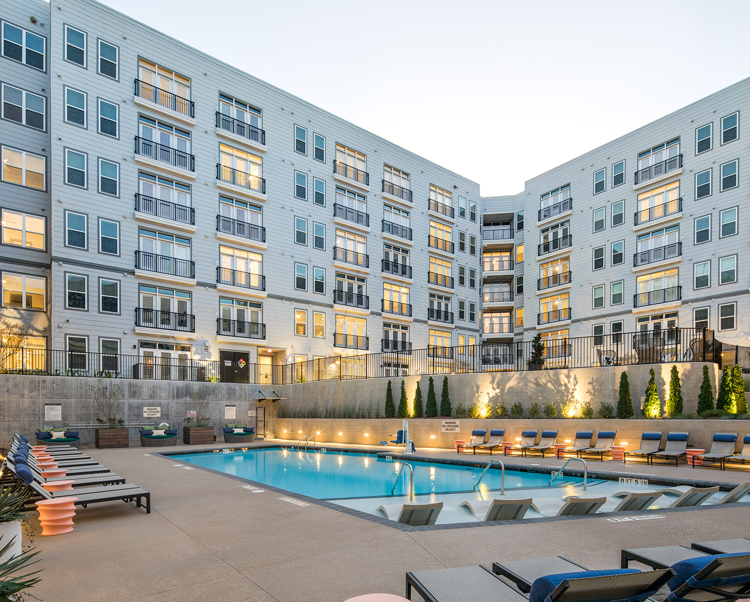 Vine North Hills pool during dusk with the lights on, lounge chairs surrounding the pool